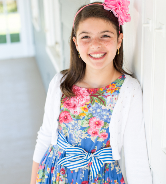 Young girl in a floral dress with a flower in her hair, smiling happily.