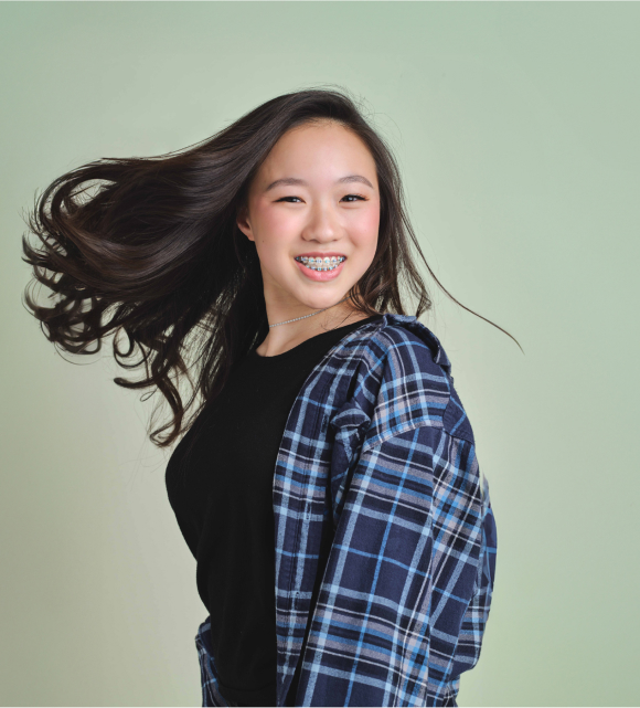 Girl with long black hair smiling brightly, showcasing her braces.