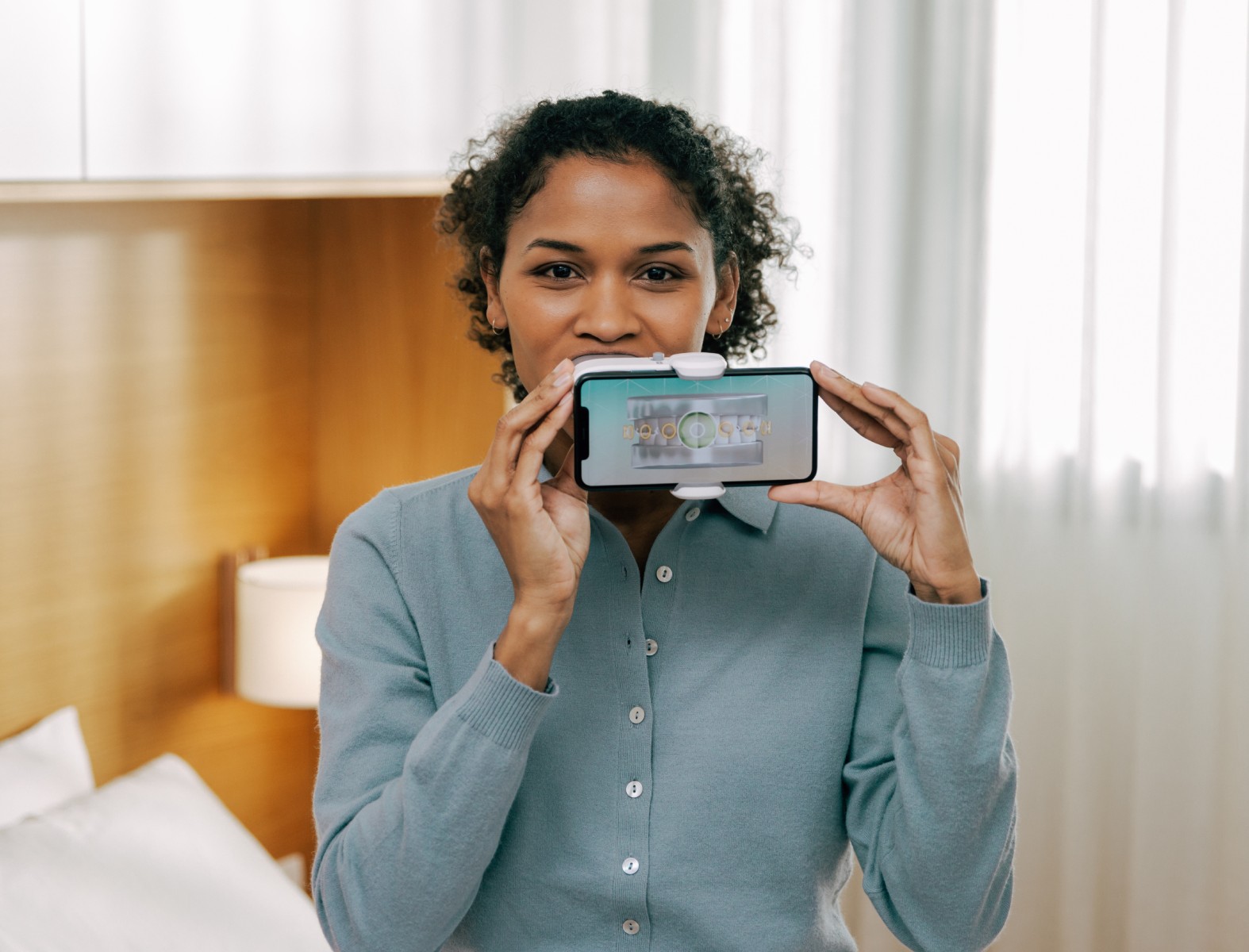 A curly-haired young woman using a dental monitoring tool with a focused expression.