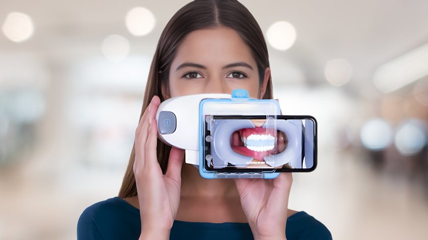 A young girl holding up a dental monitoring tool with a bright smile.