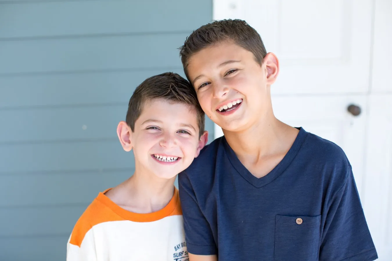 Two boys leaning on each other, both smiling happily.