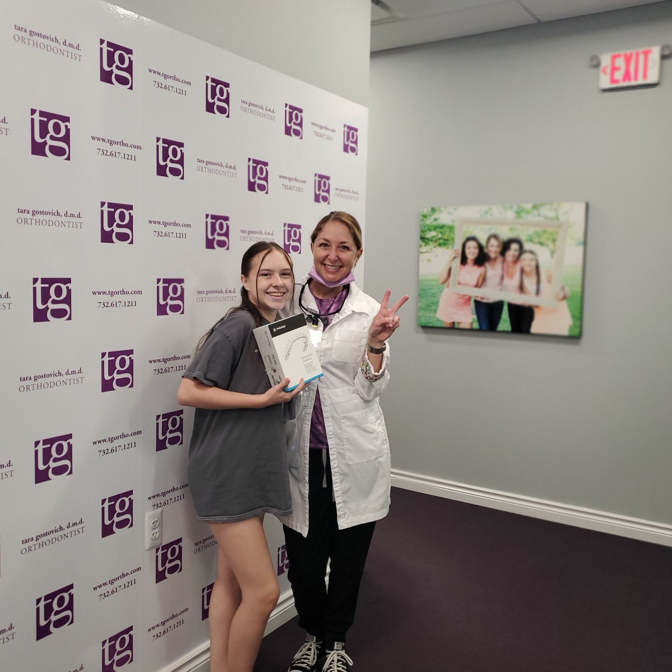 Dr. Tara giving a peace sign next to a smiling patient with braces.