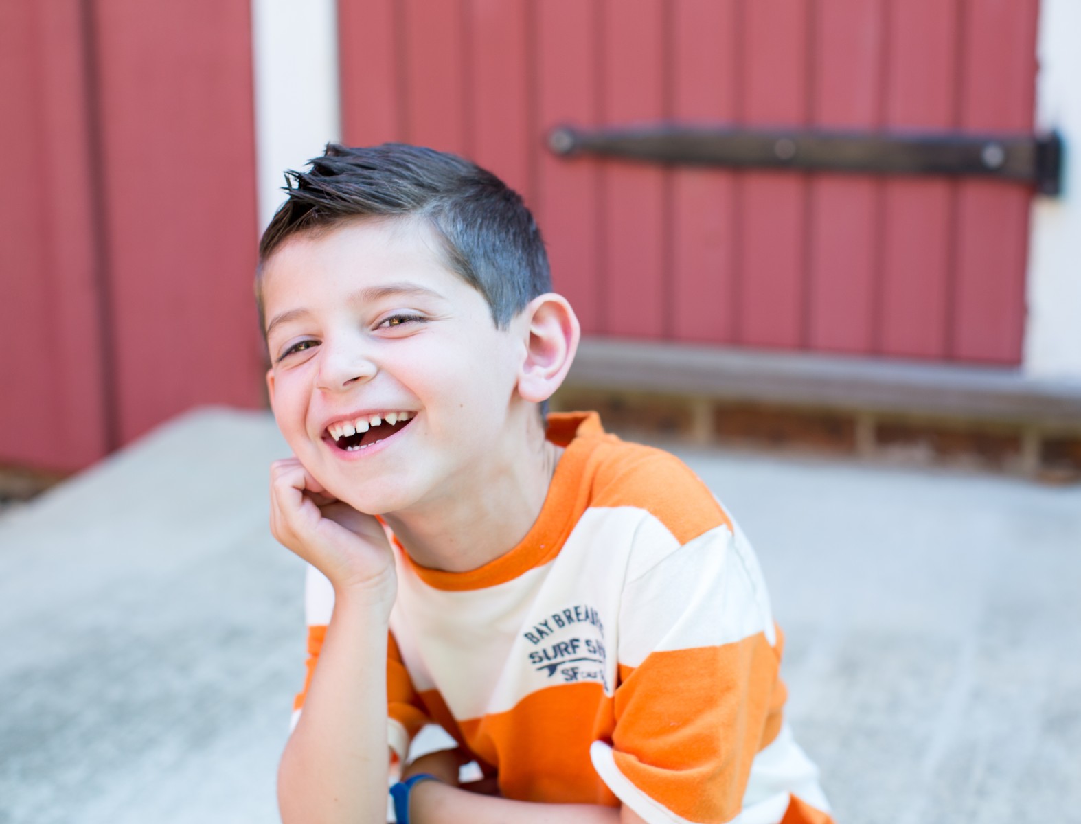 A young boy wearing an orange and white striped T-shirt, smiling brightly.