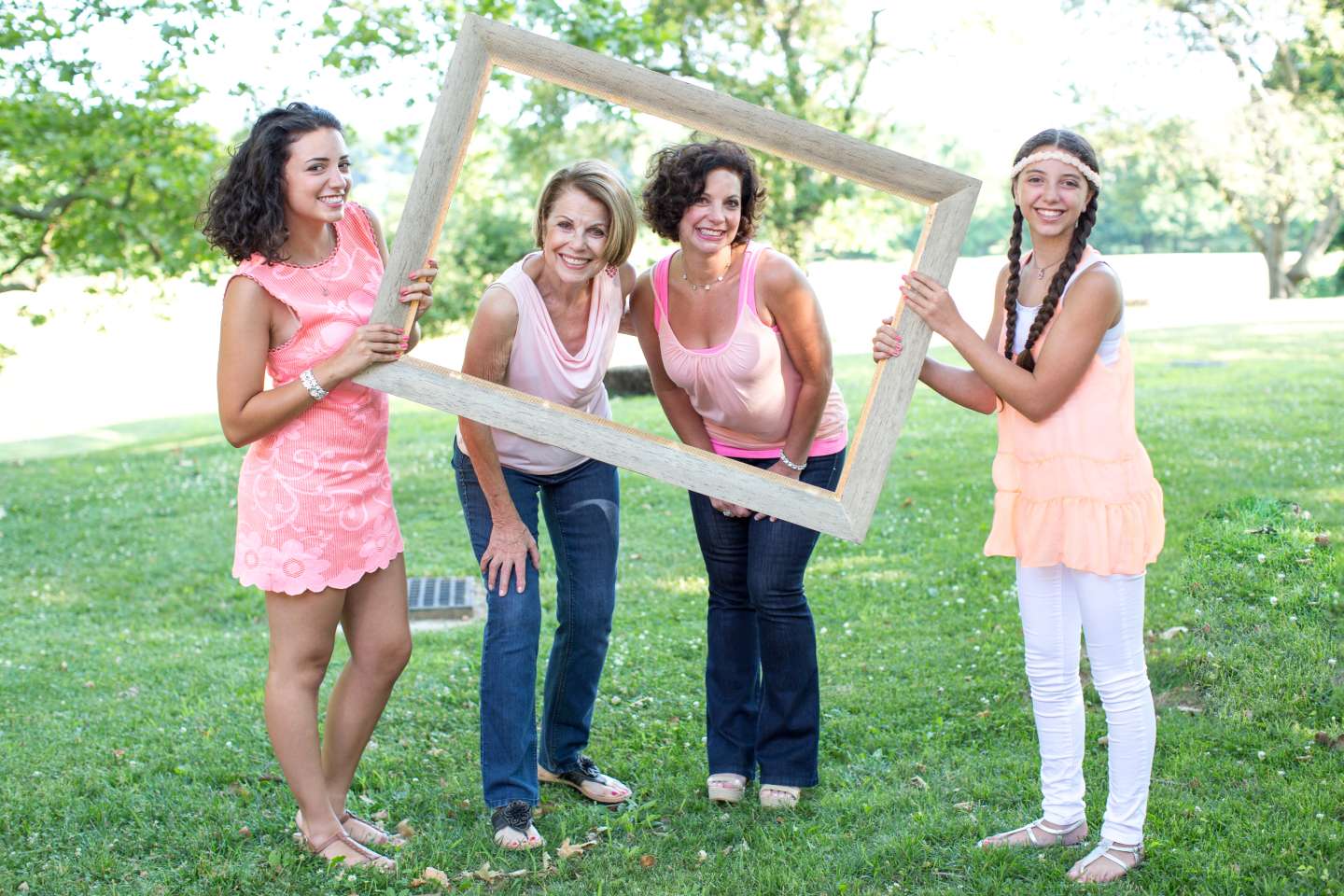 Two girls holding up a picture frame with their mothers smiling inside.