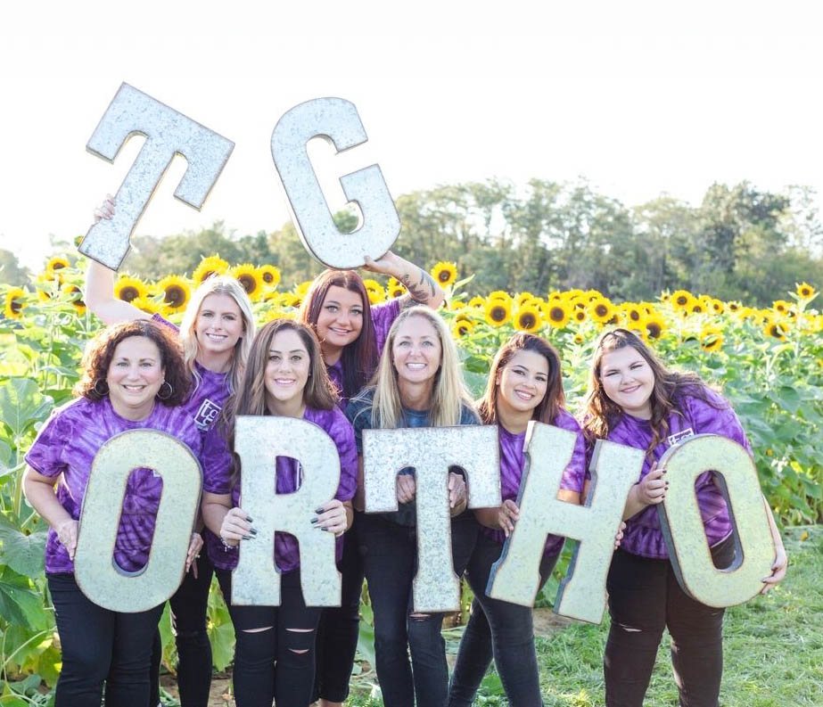 TG Ortho crew holding up letters in front of a vibrant sunflower field.