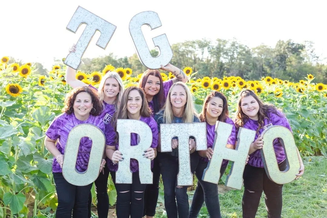 TG Orthodontics team posing together holding large letters that spell TG Ortho