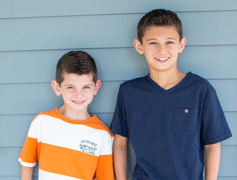 Two boys smiling broadly, showcasing their straight teeth after orthodontic treatment.