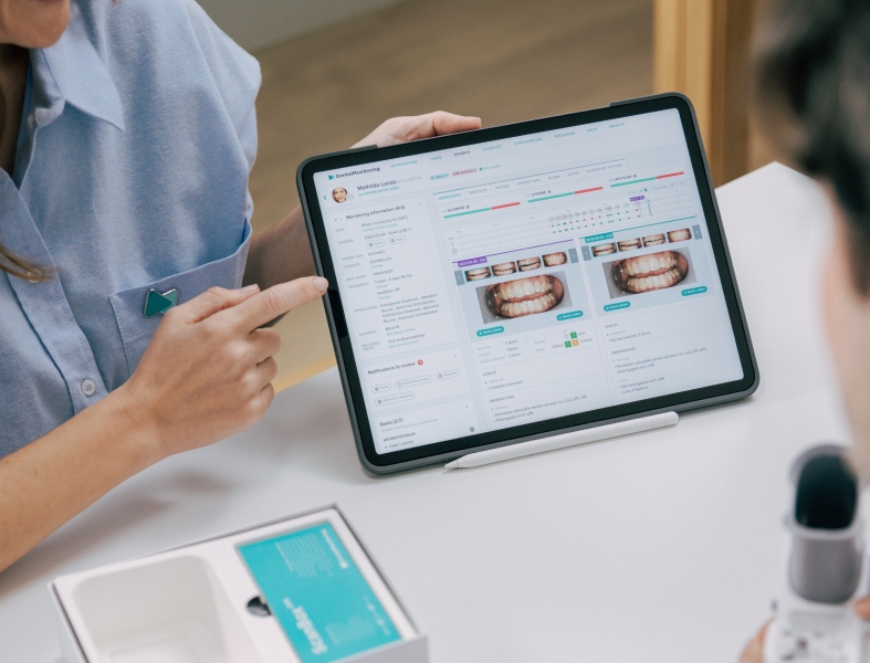 Orthodontic technician holding a tablet displaying a close-up image of a patient's teeth.