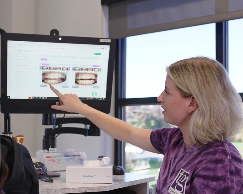 Orthodontic technician pointing at dental work displayed on a computer monitor.