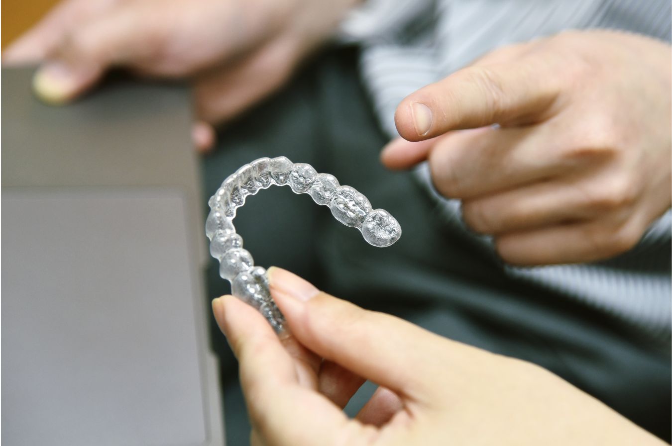 Hands holding a clear aligner while weighing Invisalign cost and payment options